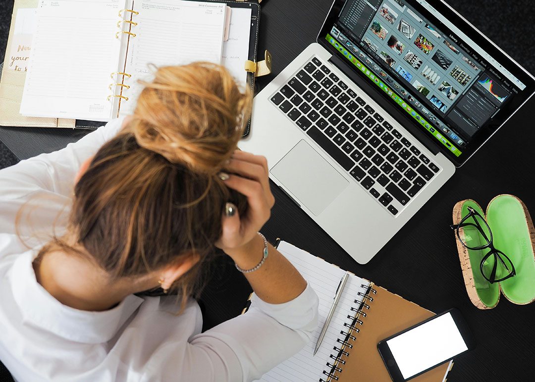 woman sitting in front of a laptop computer and holding her head in her hands like a student having a panic attack due to stress