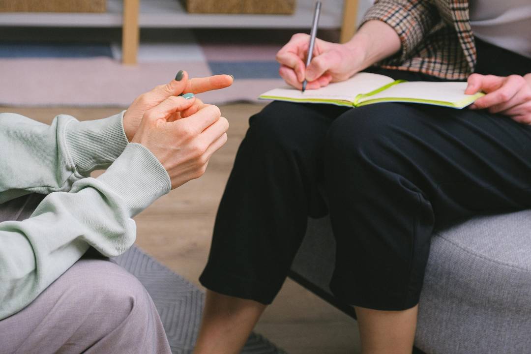 close up of two people's hands with one of them writing in a notebook