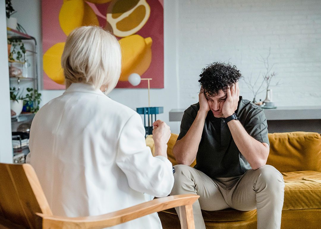 depressed man sitting in front of therapist and holding his head in his hands